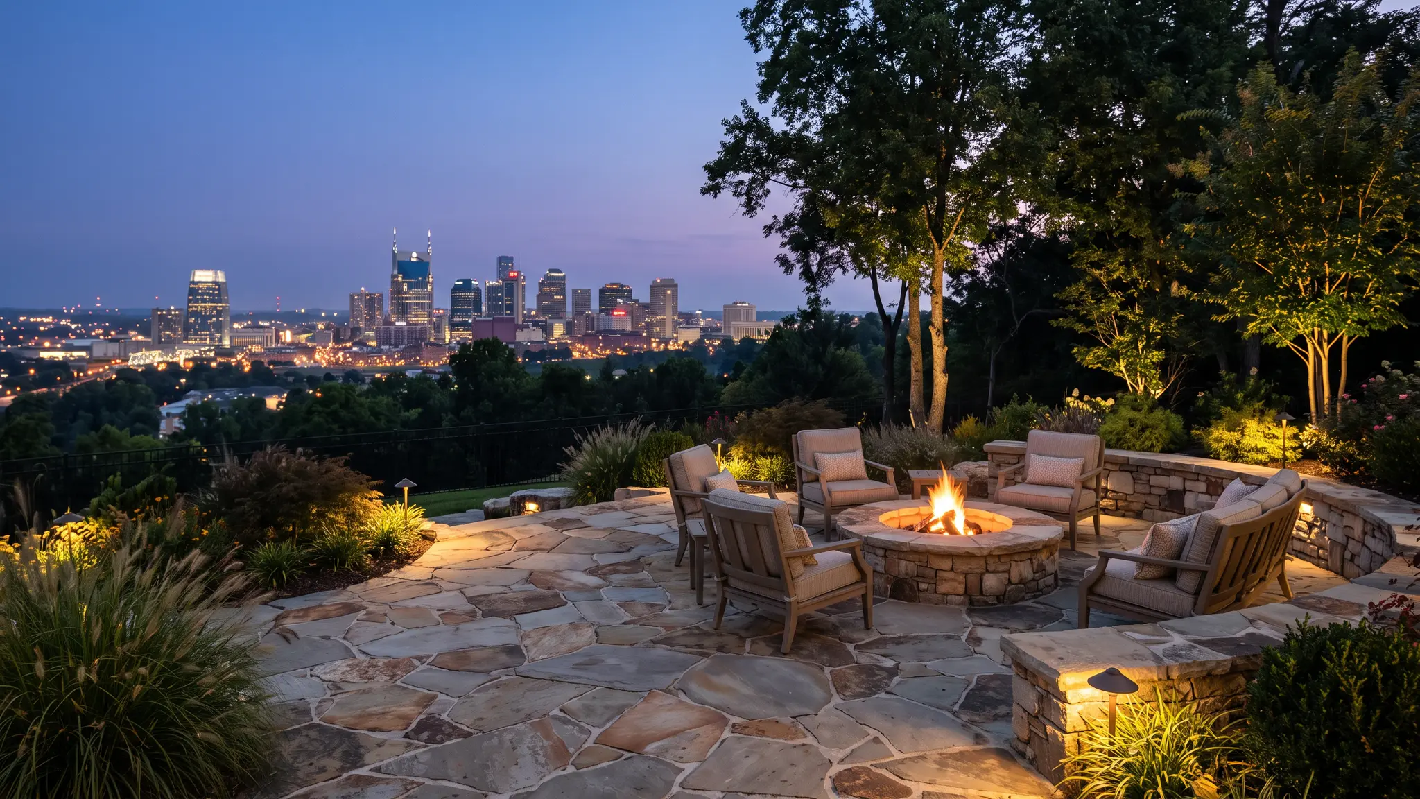 Music City Hardscape | Luxury landscaping and hardscape in Nashville, TN A luxury flagstone patio with a glowing stone fire pit and seating overlooking the Nashville skyline at dusk